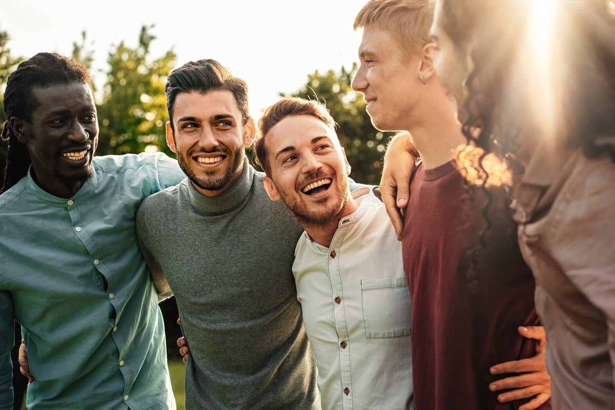 Group of diverse middle-aged men of different ethnicities laughing and bonding together outdoors, representing supportive male friendship and recovery community