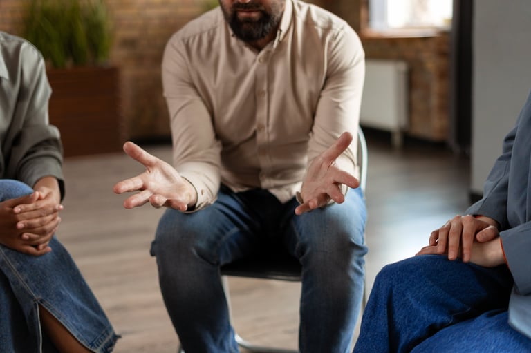Middle-aged man sharing and gesturing during group therapy session, representing peer support and open communication in recovery