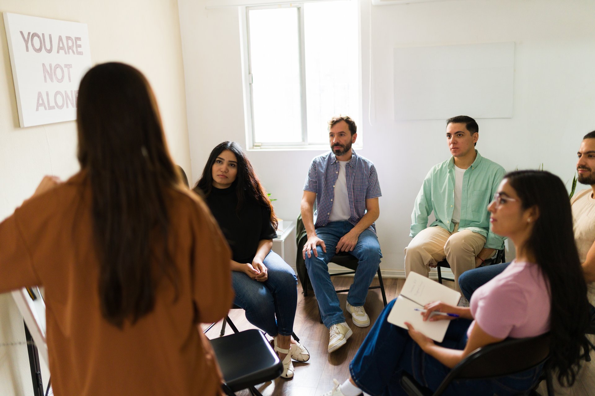 People sitting in a circle listening to counselor leading group therapy, discussing feelings and experiences for well-being