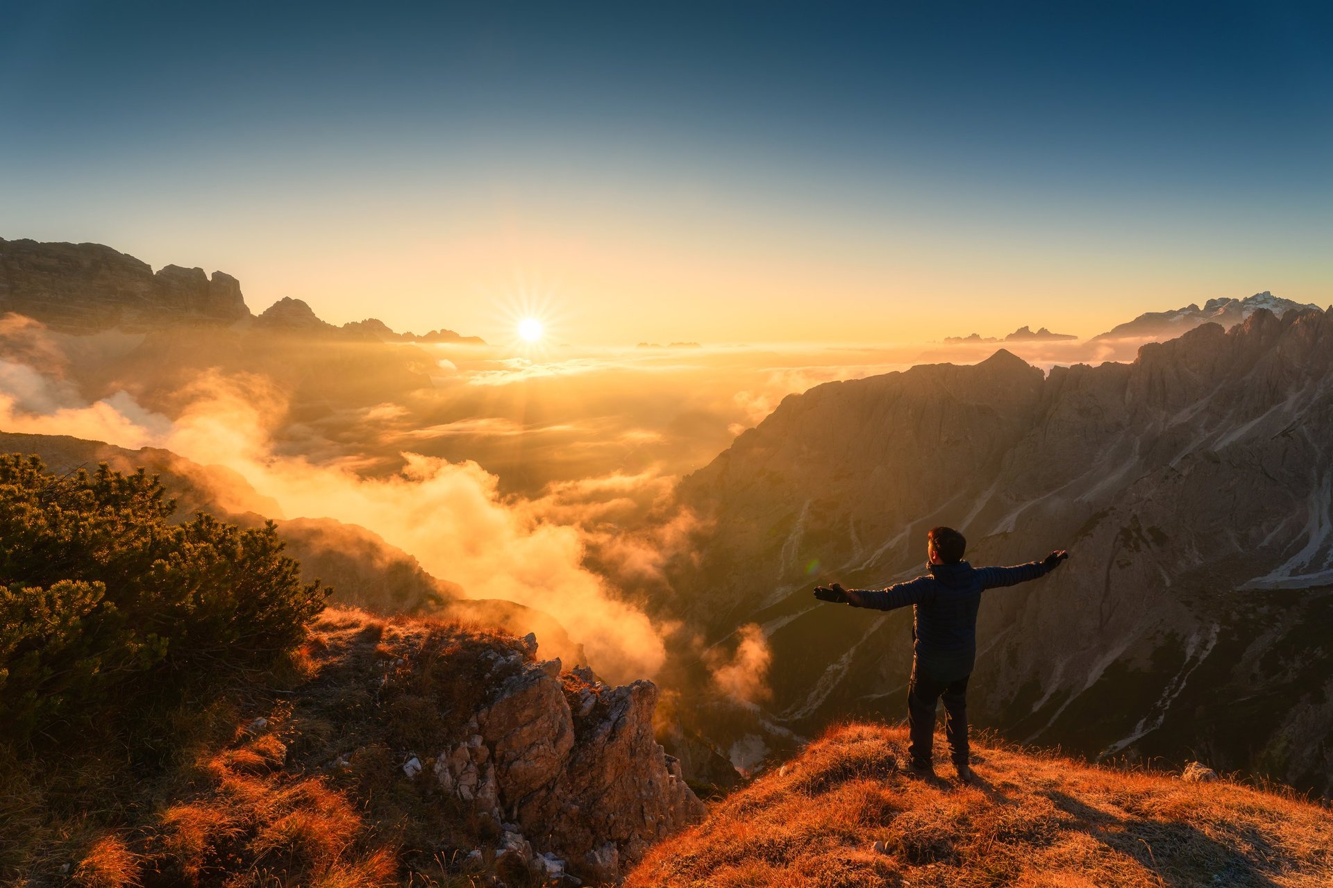 Scenic alpine landscape of golden sunrise over male traveler standing with mountain range
