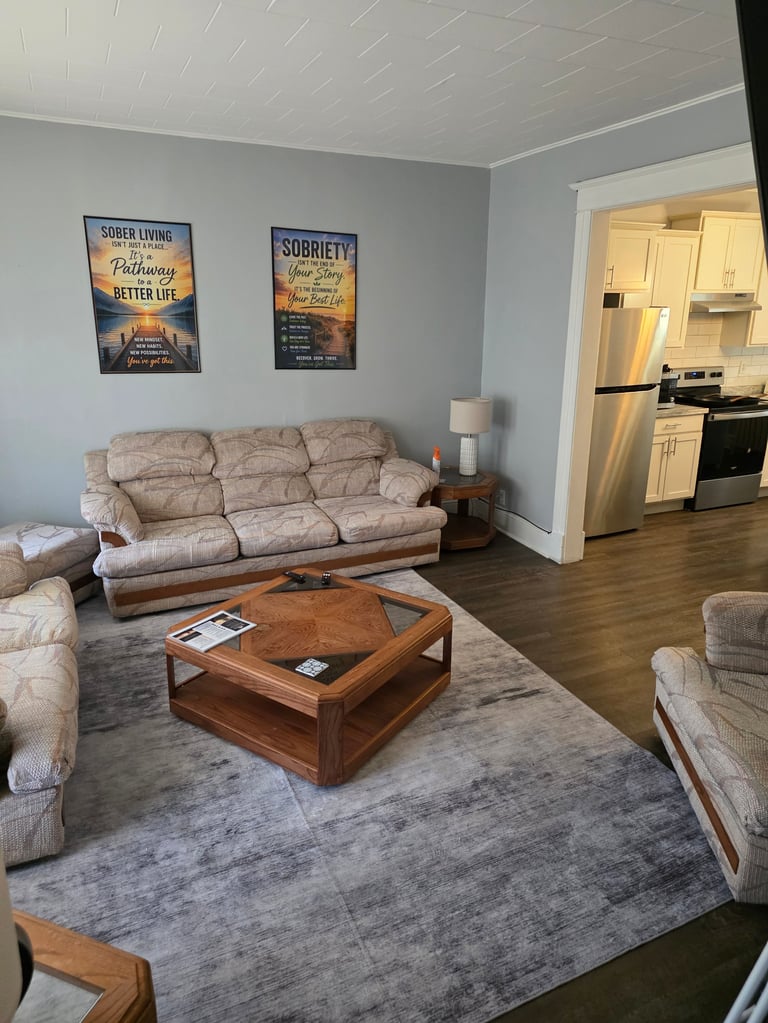 A light blue living room with beige upholstered furniture, wooden coffee table, area rug, and motivational wall art overlooking an open kitchen