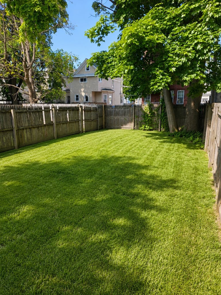 Large backyard with green lawn surrounded by wooden fences and trees, with yellow house visible in background