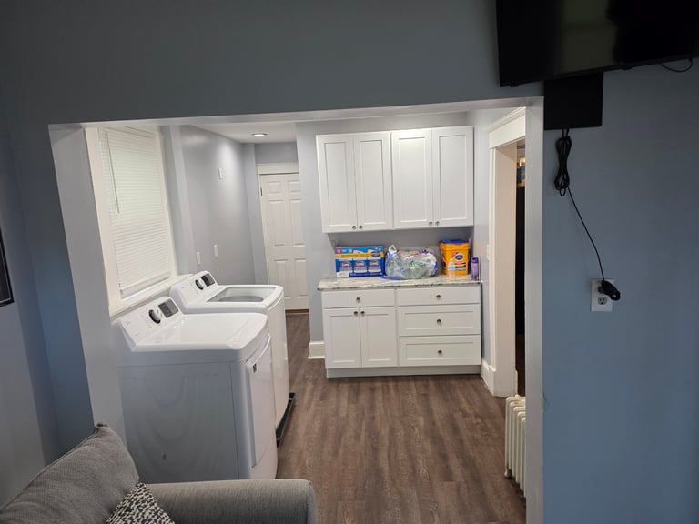 Laundry and bathroom room display with white cabinetry, washing machine, sink, and wooden flooring