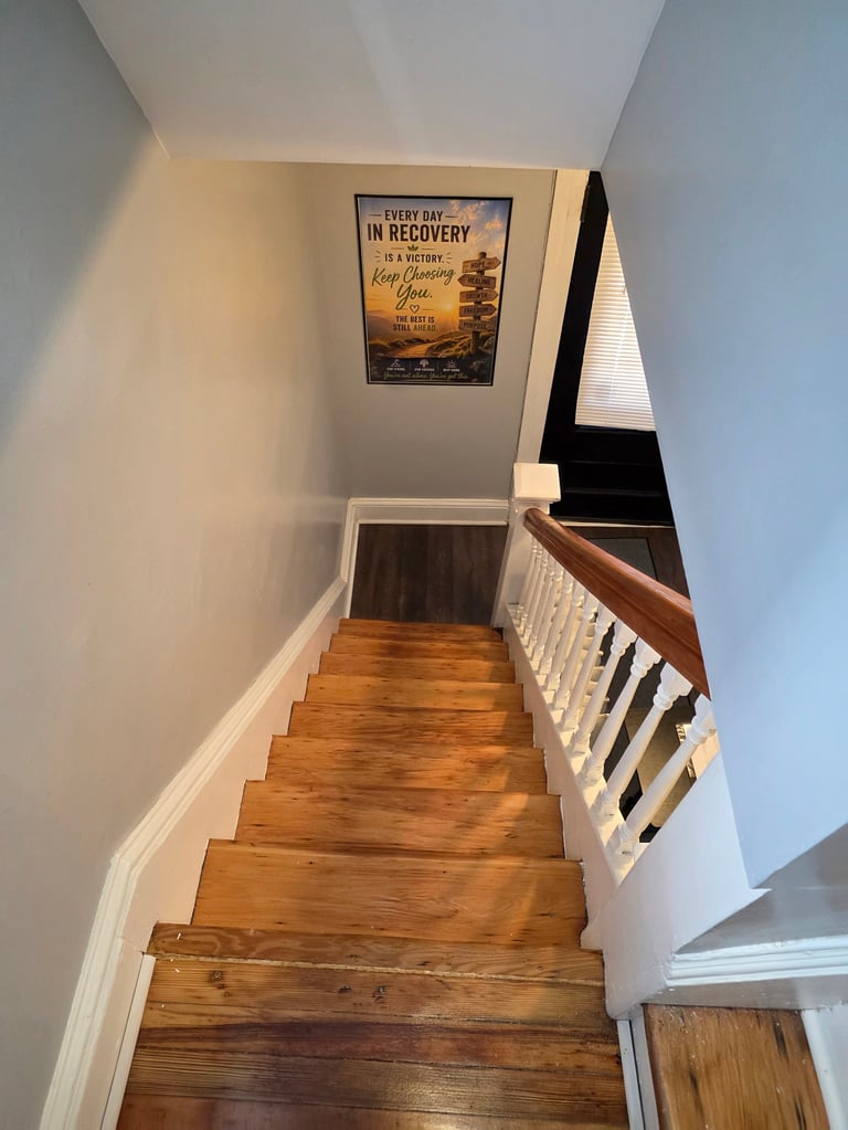 Wooden staircase descending between white walls with white balusters, motivational poster on upper wall, and hardwood flooring visible