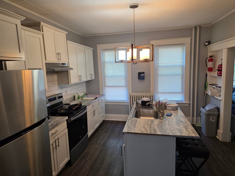 Modern kitchen with white cabinets, stainless steel appliances, gray island countertop, and large windows with blinds